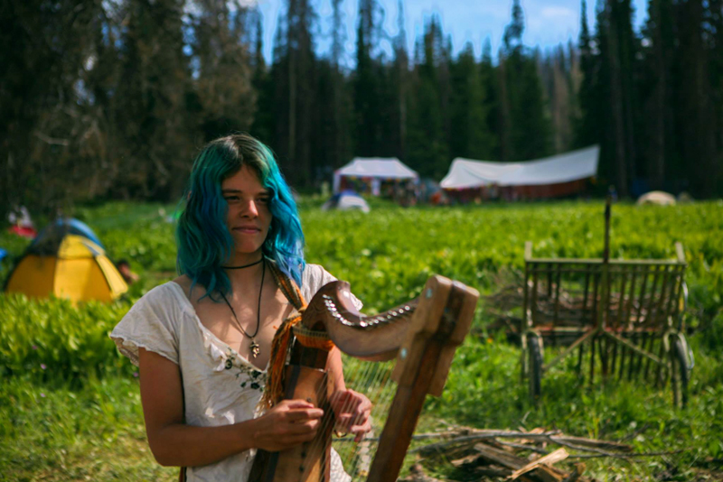 A girl playing the harp at the Rainbow Gathering in the Uinta National Forest, Utah, USA. Photo Tyler Coleman.